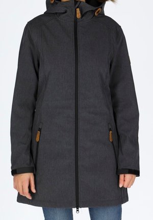 Vrouw draagt een donkergrijze winterjas met capuchon, voorrits en ritszakken, gecombineerd met blauwe spijkerbroek.