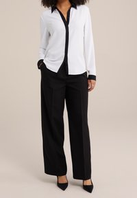 White long-sleeve button-up shirt with black collar and cuffs, paired with black wide-leg trousers and pointed black heels.