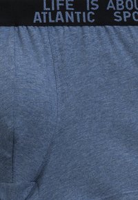 Niebezpieczne bokserki z niebieskiego melanżowego materiału z czarnym elastycznym pasem, na którym znajdują się białe napisy. Tekstura wydaje się miękka i elastyczna.