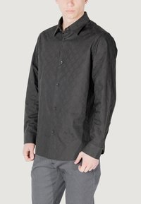 Camicia nera a maniche lunghe con motivo a diamante, con chiusura frontale a bottoni e colletto classico. Realizzata in un tessuto liscio con una sottile lucentezza.