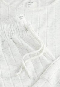 Vit loungewear-set med en strukturerad, ribbad design. Inkluderar en topp med rund halsringning och byxor med ett elastiskt midjeband och dragsko.