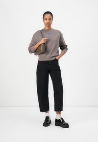 Gray sweatshirt with a blue logo, high-waisted black wide-leg jeans, layered white socks, and black chunky shoes. A textured olive handbag is held.