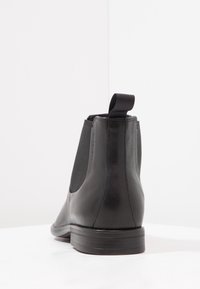 Bottes basses en cuir noir avec panneaux latéraux élastiques et languette de tirage. La surface lisse présente un bout arrondi et un talon bas empilé.