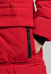 Rood geïsoleerde jas met een gladde textuur, een ritszak en geribbelde manchetten, die een modern en praktisch ontwerp benadrukt.