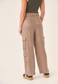 Pantalones cargo de pierna ancha beige con grandes bolsillos laterales, una textura de tela suave y una cinturilla alta con pliegues. Combinados con zapatillas de plataforma.