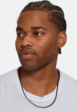 Zwarte metalen kettinghalsketting gedragen over een wit shirt, met een strak, minimalistisch ontwerp met platte schakels en een gladde textuur.