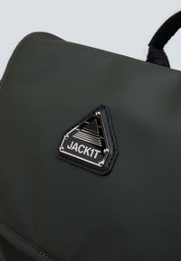 Zaino verde scuro con superficie testurizzata, toppa nera triangolare con accessori in argento e logo "JACK1T" in rilievo.