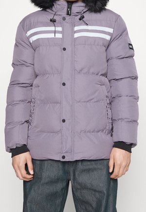 Person trägt eine fliederfarbene gesteppte Winterjacke mit schwarzer Fellkapuze, vorderen Druckknöpfen, zwei reflektierenden weißen Streifen und Seitentaschen.