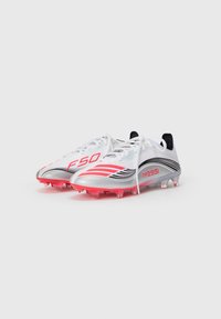 Balonų futbolo batai balti su raudonais ir juodais akcentais, su "F50" ir "Messi" prekinių ženklų ženklais, permatomomis raudonomis dygliuotomis padais ir baltais raiščiais.