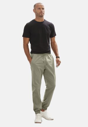 Zwarte korte mouwen t-shirt, licht olijfgroen drawstring broek en witte sneakers. Casual fit, elastische manchetten op de broek.