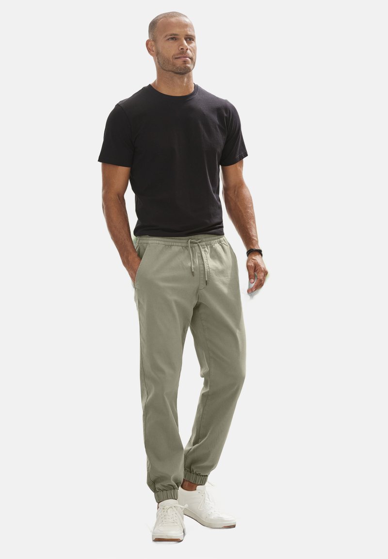 Zwarte korte mouwen t-shirt, licht olijfgroen drawstring broek en witte sneakers. Casual fit, elastische manchetten op de broek.