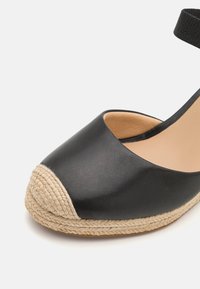 Svarta läderespadriller med rundad tå, med en vävd jutesula och ett ankelsnöre, vilket ger kontrasterande texturer.