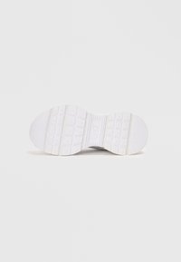 Hvit sneaker-såle med teksturert gummi. Egenskaper inkluderer et mønstrete slitedekk for grep, og et rektangulært design for stabilitet.