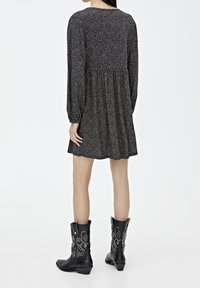 Czarna sukienka w kwiaty z długimi rękawami i marszczonym pasem, połączona z czarnymi kowbojkami z detalicznym haftem i niskim obcasem.