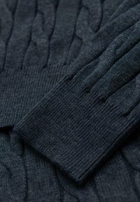 Pull en velours marine foncé avec un motif en tricot à torsades, des poignets côtelés et une finition texturée. Le matériau semble doux et épais.
