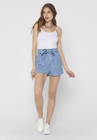 Light blue denim shorts with a belted waist, featuring two front pockets, a relaxed fit, and a frayed hem. Paired with a white tank top.