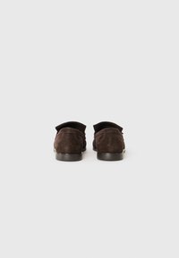Bruine suede instappers met een lage hak, voorzien van een zachte textuur en een minimalistisch ontwerp. De achterkant toont de gebogen vorm en de stiksels.