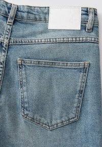 Lichtblauwe denim jeans met een achterzak, zichtbare stiksels en een rechthoekig wit etiket op de tailleband. Zachte textuur.