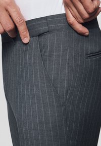 Szare spodnie w prążki z płaskim przodem, z boczną kieszenią i dopasowanym krojem. Teksturowany materiał o gładkim wykończeniu.
