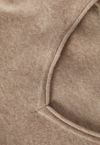 Tessuto lavorato a maglia di colore marrone chiaro con una texture morbida. Presenta un colletto rotondo e un orlo pulito, evidenziando la sua qualità morbida e traspirante.