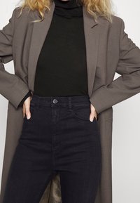 Gray blazer over a black turtleneck and dark high-waisted jeans. Blazer features wide sleeves; jeans have a smooth texture and button closure.