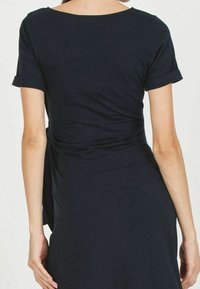 Mörkblå klänning i mjukt tyg, med korta rullade ärmar och samlad detalj i midjan, vilket skapar en figurnära silhuett.