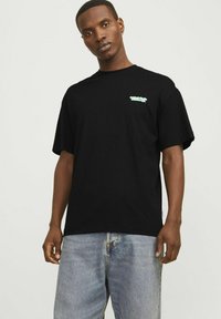 Camiseta de algodón negra de manga corta, con un pequeño logotipo verde claro en el pecho. Llevada con pantalones cortos de mezclilla azul desgastados.
