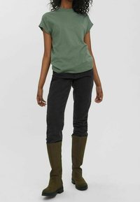Zelené bavlněné tričko s krátkým rukávem spárované s černými skinny džíny a olivově zelenými vysokými botami, které mají čistý design a volný střih.