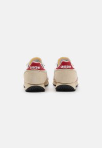 Saucony-sko med overdel i beige semsket skinn, hvite lærdetaljer, røde hællogoer og svart gummisåle, med et klassisk atletisk design.