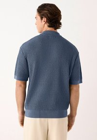 Polo cu mânecă scurtă din tricot texturat de culoare albastră, cu guler și manșete ribonate. Prezintă modele de riburi orizontale și verticale.