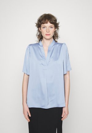 Blusa azul-claro de manga curta em tecido de satin suave, com uma pala frontal parcial e detalhes suaves com franzido nos ombros.