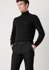 Melnā turtleneck džemperis mīkstā adījumā, saskaņots ar melniem biksēm ar pogu aizdari un sānu kabatām. Vienkāršs dizains, pieguloša silueta.