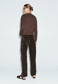 Maglione corto marrone, pantaloni di velluto marrone scuro e sandali neri con lacci. Texture liscia, design aderente e stile informale.
