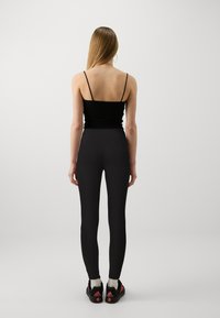Leggings neri attillati abbinati a una canotta nera con spalline sottili. Completano l'outfit delle sneakers nere con dettagli rossi.