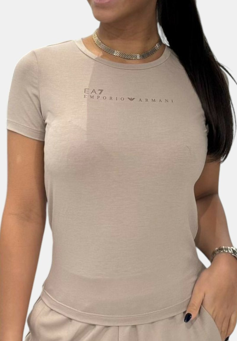 Camiseta ajustada beige de manga corta, con el logo de EA7 Emporio Armani impreso en un tono más oscuro en el pecho. Textura suave.
