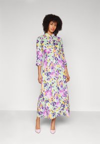 Vestido maxi floral com frente abotonada, apresentando cores pastel como verde, rosa e amarelo. Mangas longas, tecido leve e design fluído.