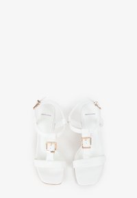 Hvide højhælede sandaler med firkantet tådesign, glatte læderremme, justerbar ankelspænde og udsmykninger i guld-tone hardware.