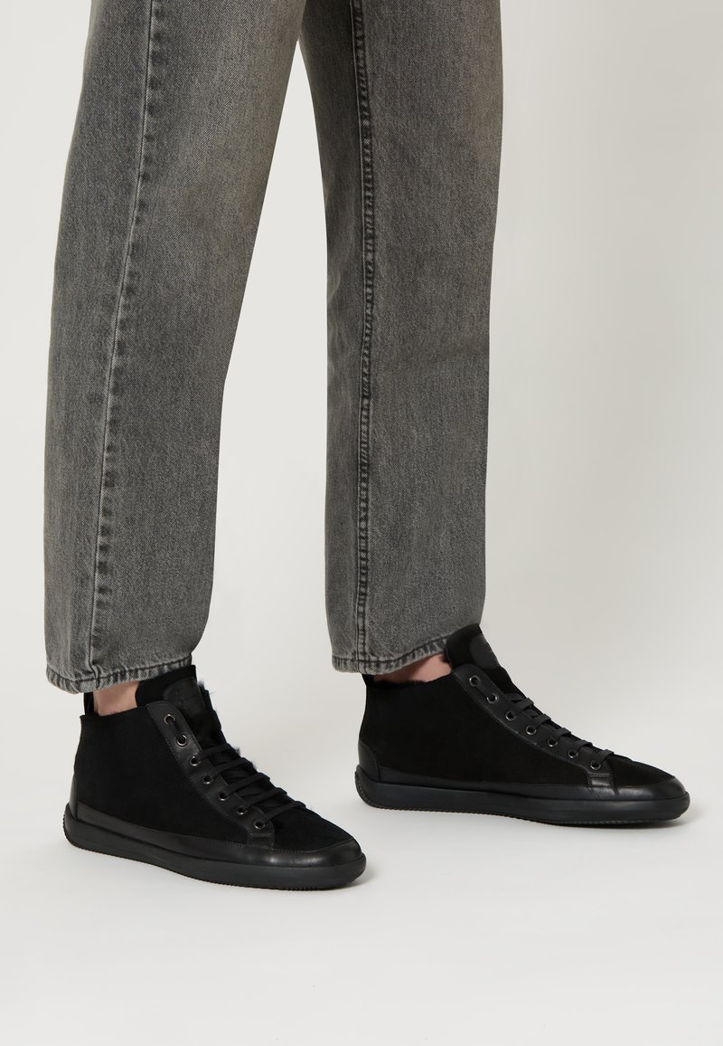 Sneaker alte nere in suede con suole in gomma, caratterizzate da un design con lacci e dettagli minimalisti neri. Indossate con jeans grigi scoloriti.