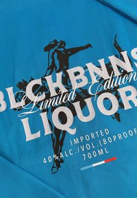 Blauwe stof met zwarte grafische afbeeldingen van dansers, met witte tekst: "BLCKBNNS Limited Edition LIQUOR," 40% Alc./Vol., 700mL.
