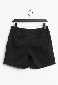 Svarta avslappnade shorts hänger på en svart galge, två bakfickor med kant, liten flagglogo på höger ficka, enkel vit bakgrund.