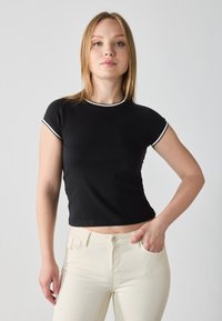Black short-sleeve, cropped t-shirt with white trim along the collar and sleeves. Worn with light-colored fitted trousers.