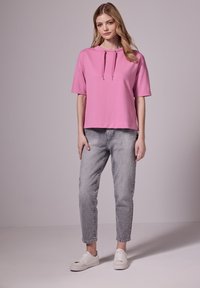 Růžová mikina s krátkým rukávem a stahovacími šňůrkami; zkombinováno se šedými tapered džíny a bílými teniskami. Jednoduchý design a pohodlný střih.