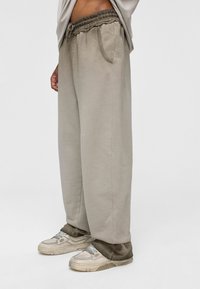 Lichtbeige wijde sweatpants met elastische tailleband, zijzakken en een zachte katoenmix textuur, gecombineerd met lichtgrijze sneakers.