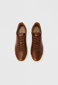 Baskets en cuir marron avec une finition lisse, dotées de lacets ronds, d'une semelle en caoutchouc beige et d'un logo doré sur la langue.