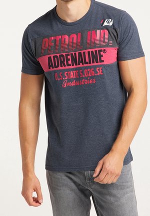 Navy sininen puuvillapaita, jonka rinnassa on rohkea punainen graafinen printti, jossa lukee "PETROL IND. ADRENALINE". Paidassa on lyhyet hihat ja pyöreä kaula-aukko.