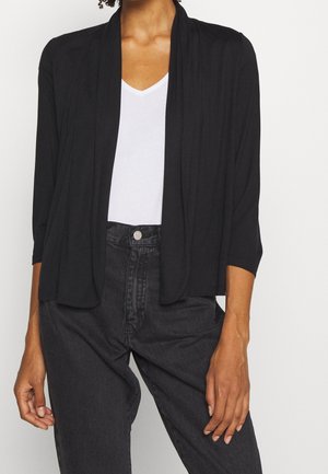 Cardigan noir ouvert à l'avant en matériau léger, avec des manches trois-quarts et une coupe décontractée, superposé sur un haut blanc à col en V.