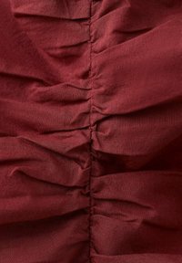 Gros plan de tissu rouge foncé rassemblé et cousu verticalement créant des plis et des rides texturées.