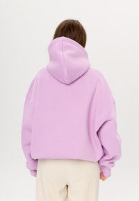 Felpa con cappuccio oversize in lavanda chiaro, con una texture morbida, spalle scese e polsini a costine, abbinata a pantaloni di colore chiaro.