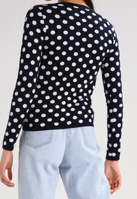 Navy sweater with white polka dots, long sleeves, round neckline, and soft texture, paired with light blue jeans, visible rear view.