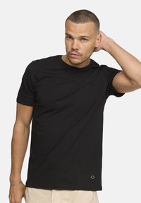 T-shirt en coton noir avec col rond, manches courtes, coupe ajustée et un petit logo géométrique en bas de l'ourlet.